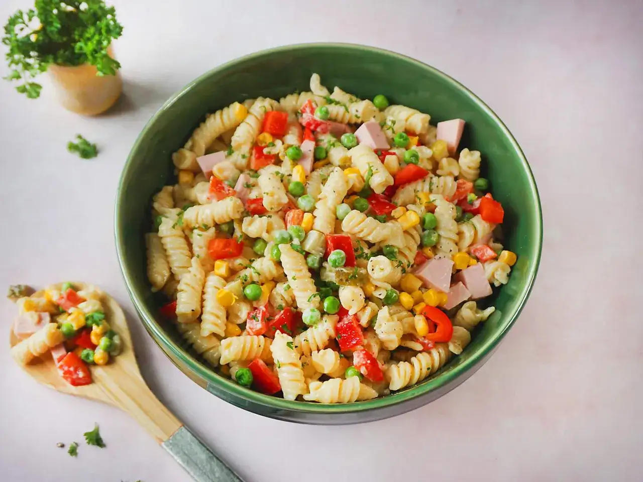 Ein bunter nudelsalat mit fleischwurst, Erbsen, Mais und Paprika in einer grünen Schüssel.