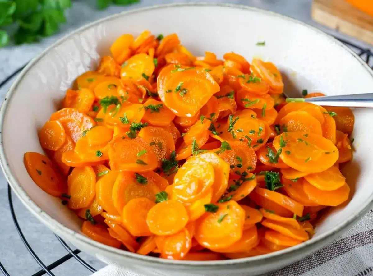 Sch&uuml;ssel mit leuchtend orangefarbenen, in Scheiben geschnittenen Karotten, garniert mit frischer Petersilie. Perfekt gekochte Karotten, die Lust auf mehr machen.