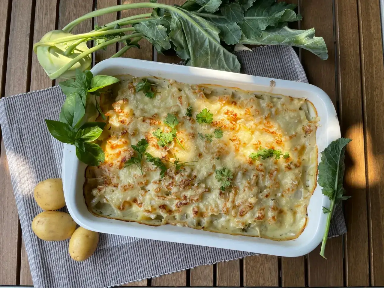 Herzhafter Kohlrabi Kartoffel Auflauf mit Käse überbacken, garniert mit Petersilie und frischem Basilikum.