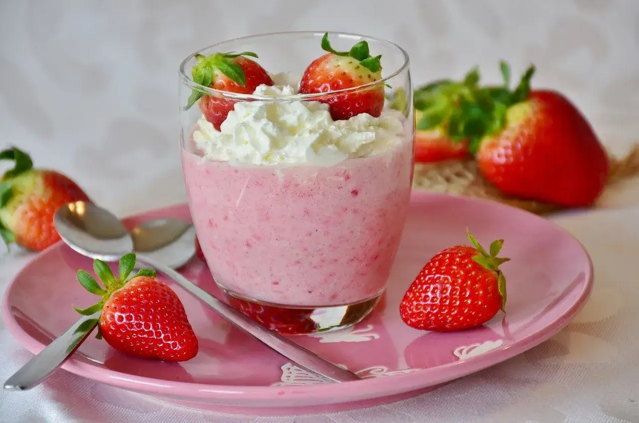 Ein Glas mit einem schnellen Dessert mit Quark und Joghurt, garniert mit Schlagsahne und frischen Erdbeeren.