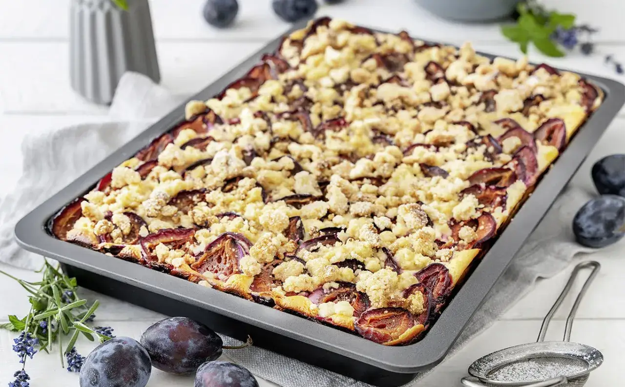Frisch gebackener Zwetschgenkuchen vom Blech mit Streuseln, garniert mit frischen Zwetschgen und Kräutern.