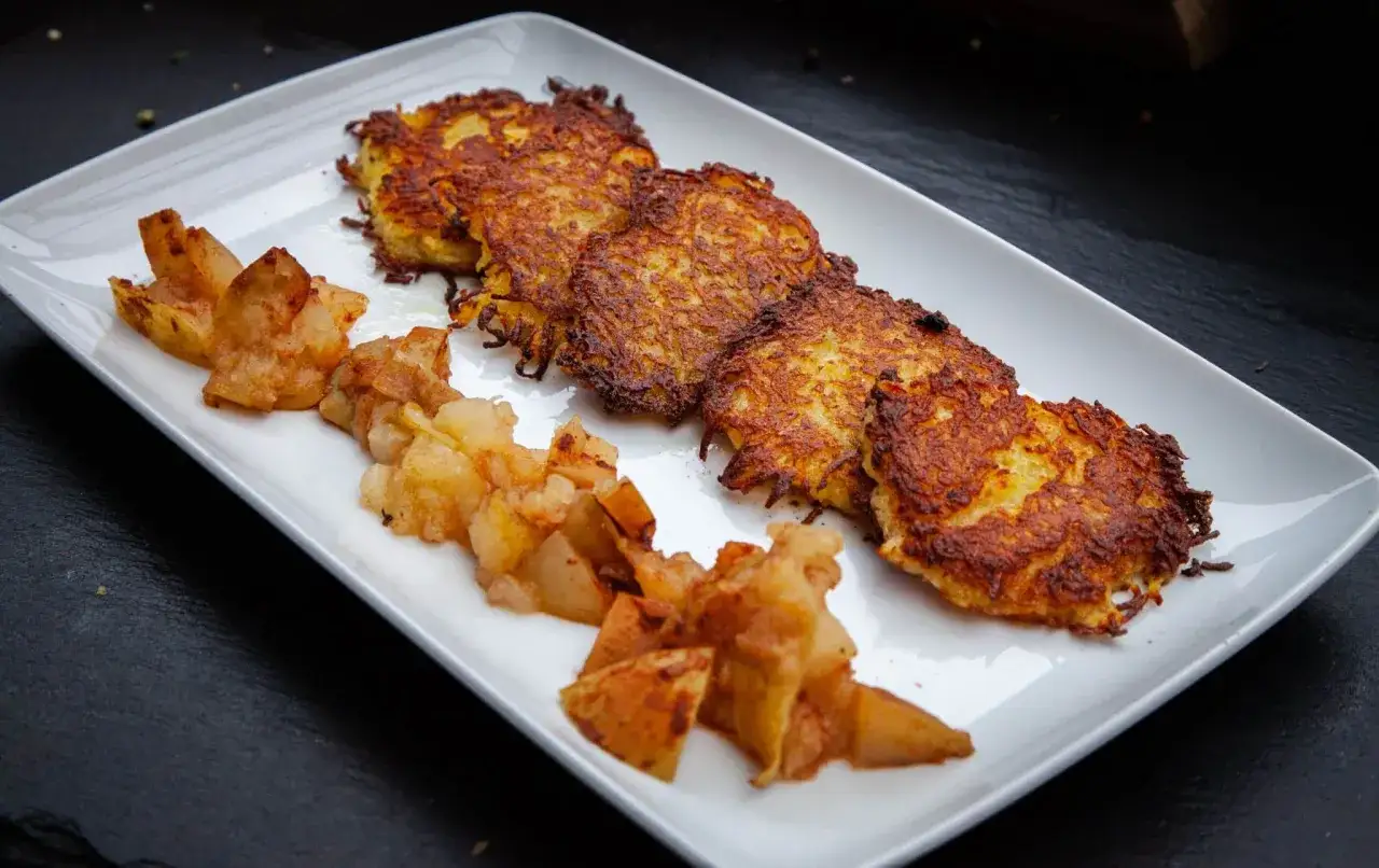 Knusprige Kartoffelpuffer mit Apfelmus auf einem weißen Teller.
