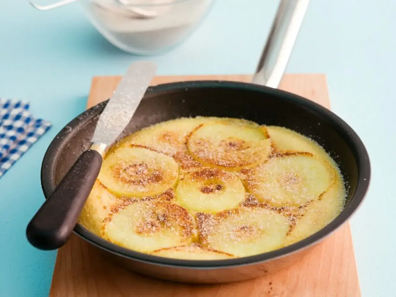 Ein goldbrauner Apfelpfannkuchen im Pfännchen, bestreut mit Zucker. Ein köstliches Apfelpfannkuchen Rezept zum Genießen.