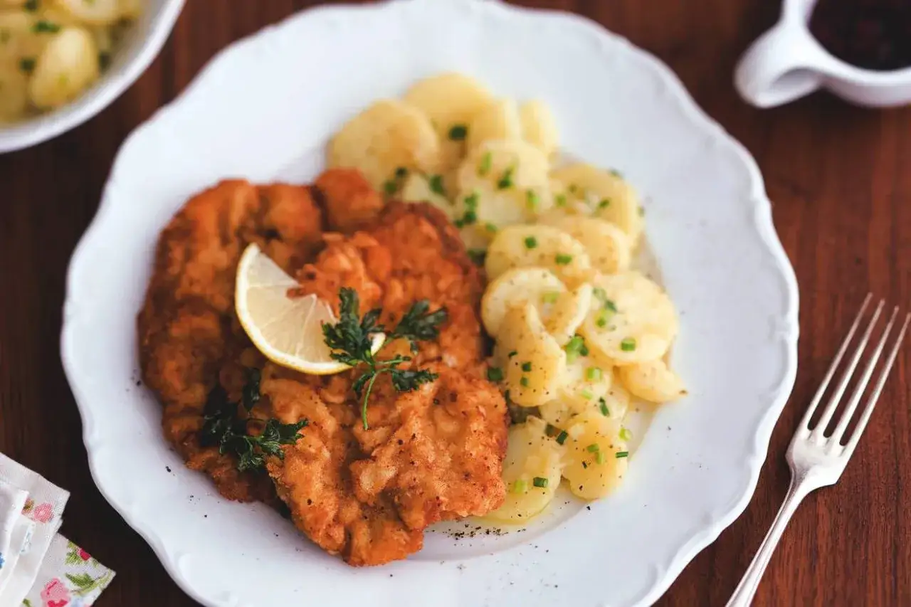 Zwei goldbraune Wiener Schnitzel mit Zitrone und Petersilie, serviert mit Kartoffelsalat.