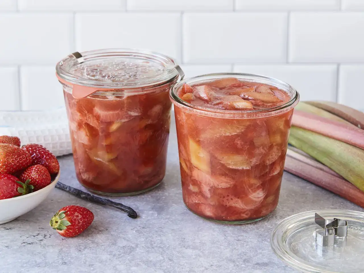 Zwei Gläser mit leckerem Rhabarberkompott, daneben frische Erdbeeren und Rhabarberstangen.