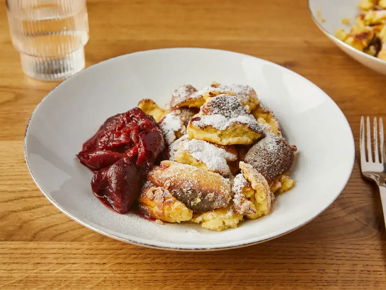 Ein Teller mit Kaiserschmarrn, bestäubt mit Puderzucker, und dazu eine Portion Zwetschgenröster. Ein köstliches Kaiserschmarrn Rezept zum Genießen.