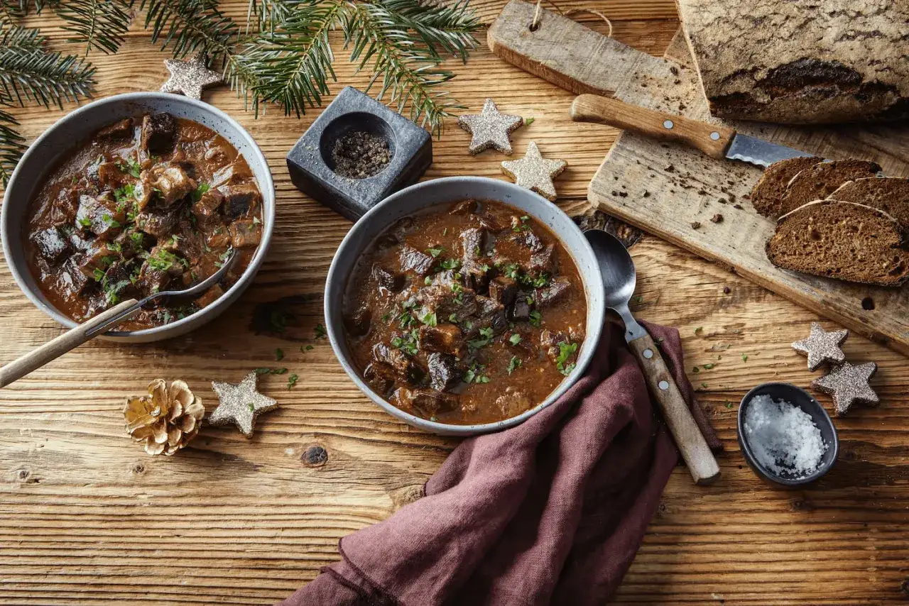 Herzhaftes Gulasch im Schnellkochtopf, garniert mit Petersilie, serviert mit Brot und Salz.