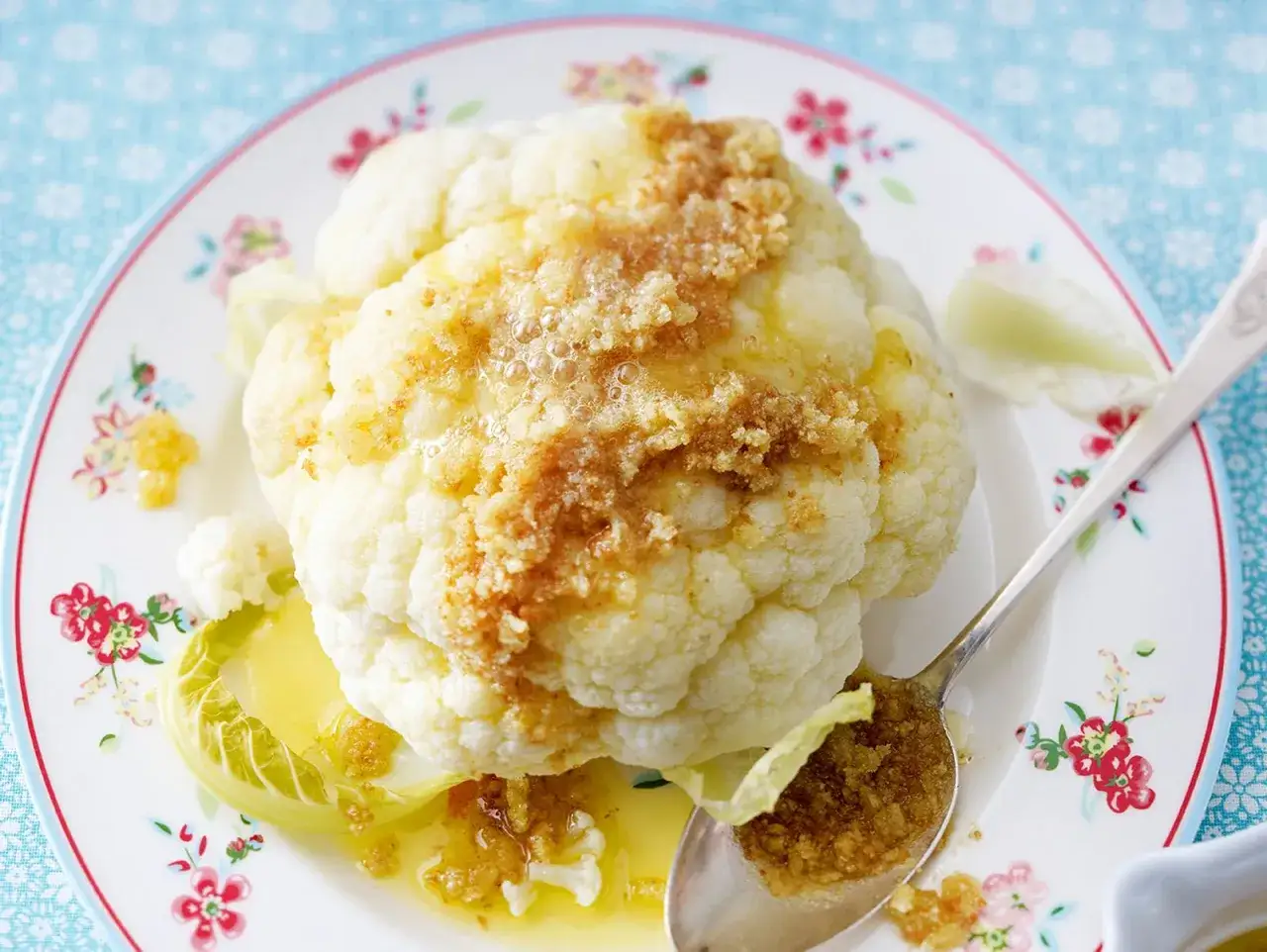 Ganzes Blumenkohl-Rezept mit Butter und Krüutern, serviert auf einem Teller mit Blumenmuster.