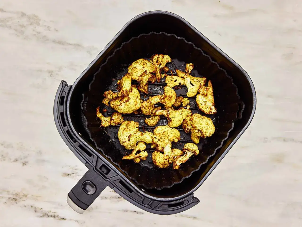 Gebratener Blumenkohl mit Gewürzen in einem Airfryer-Korb, bereit zum Genießen.