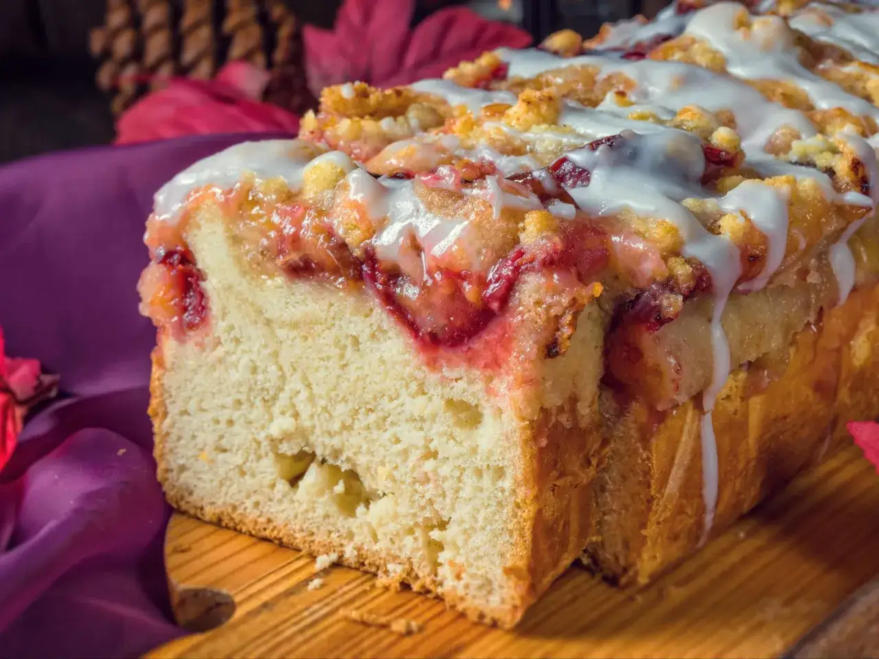 Saftiger Pflaumenkuchen in Kastenform, mit Streuseln und Zuckerguss, auf einem Holzbrett, umgeben von Herbstlaub.