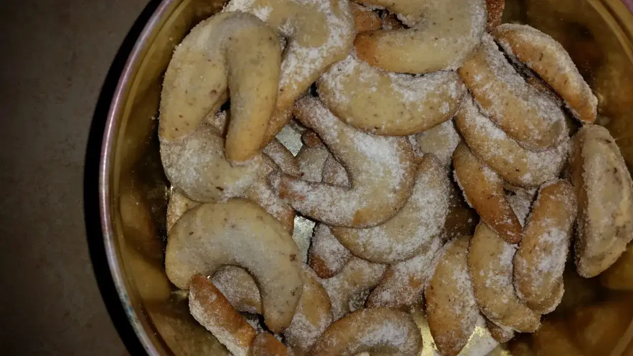 Ein goldener Blechbehälter gefüllt mit vielen Vanillekipferln, bestäubt mit Puderzucker.