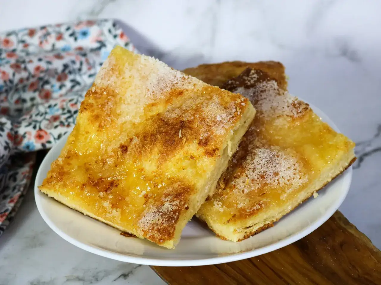 Zwei Stücke goldbrauner Zuckerkuchen, bestreut mit Kristallzucker, auf einem Teller. Ein einfaches, leckeres zuckerkuchen rezept.