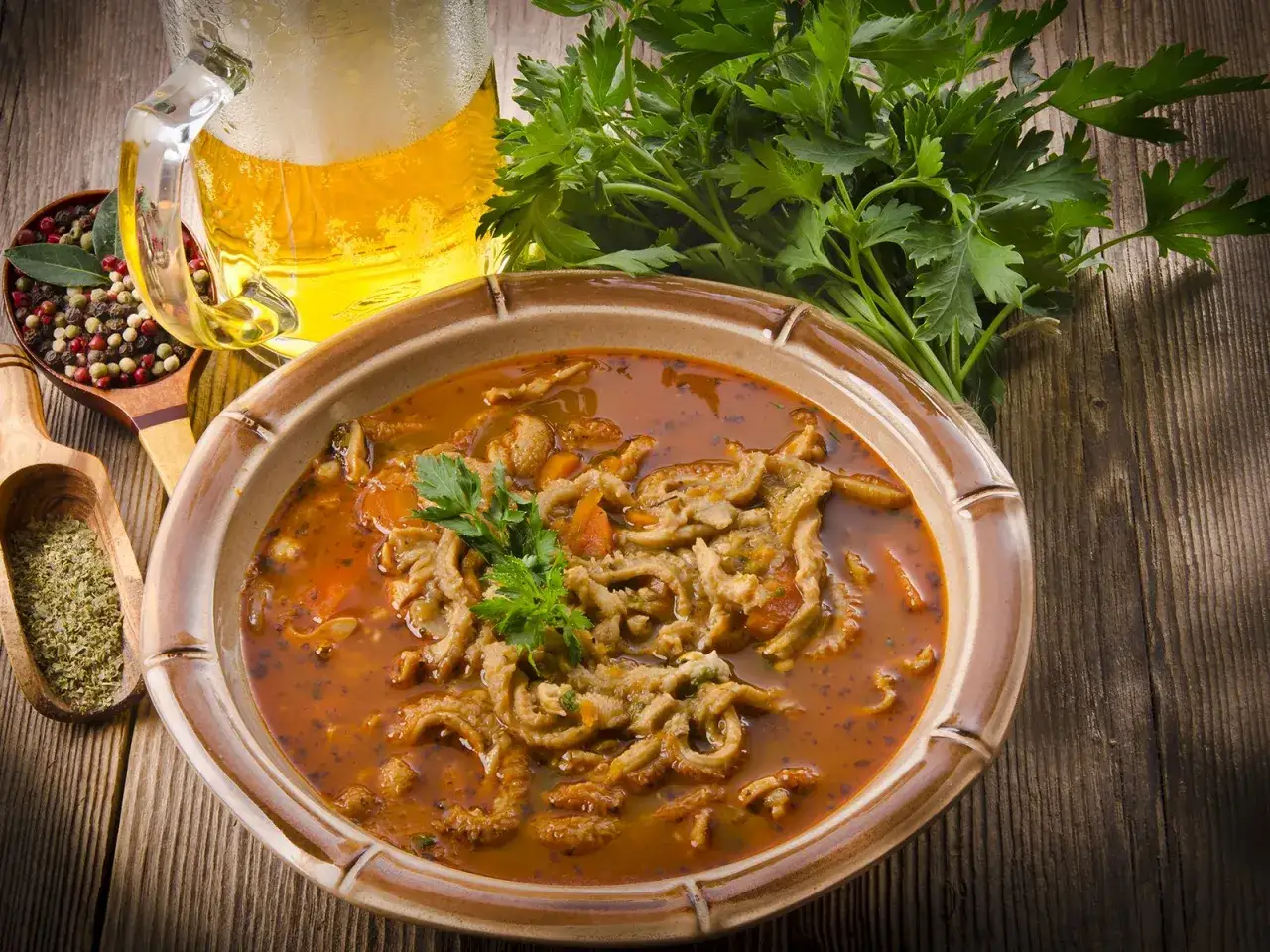 Herzhaftes Kutteln Rezept in einer Schüssel, garniert mit Petersilie. Daneben ein Glas Bier, Gewürze und Kräuter.