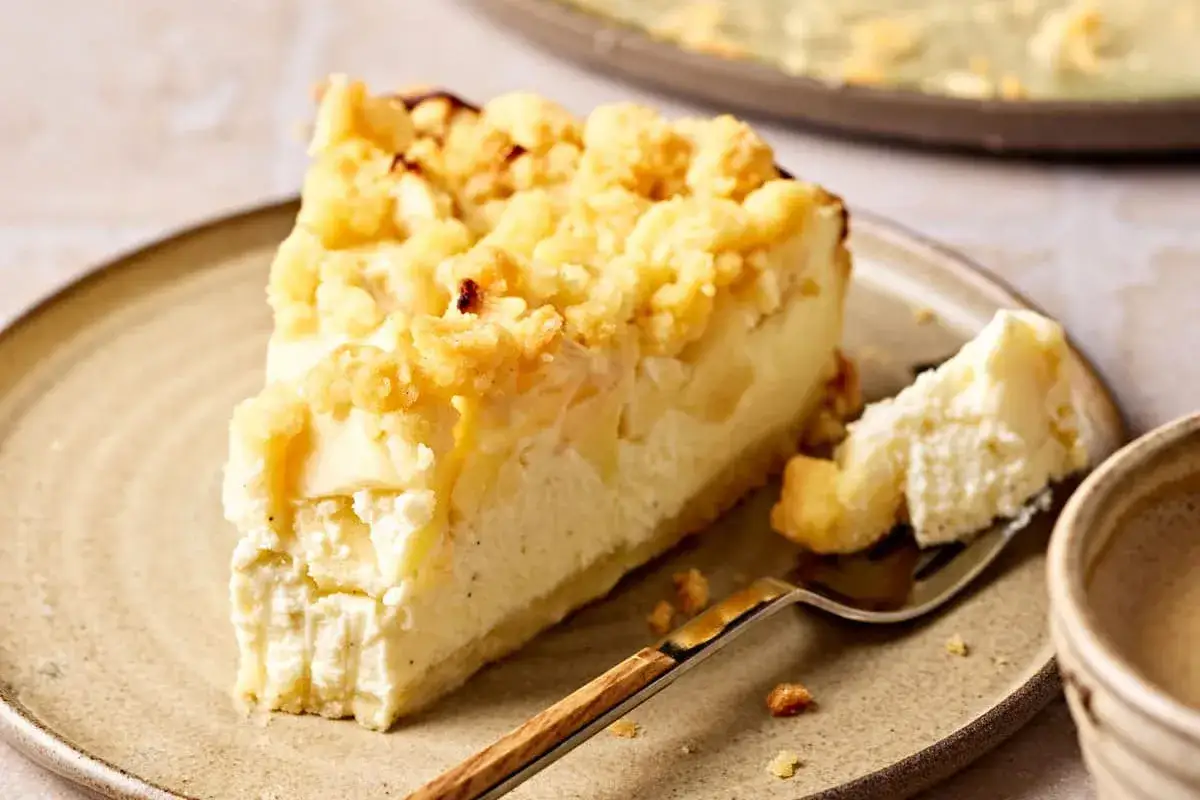 Ein Stück Apfel Quark Kuchen mit Streuseln auf einem Teller. Ein Stück wurde mit einer Gabel abgetrennt.