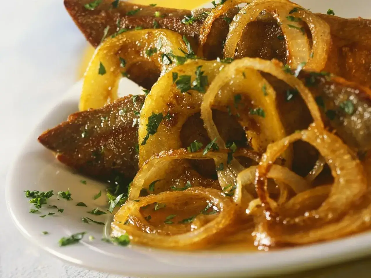 Gebratene Leber mit karamellisierten Zwiebelringen, ein klassisches leber rezept, garniert mit Petersilie.