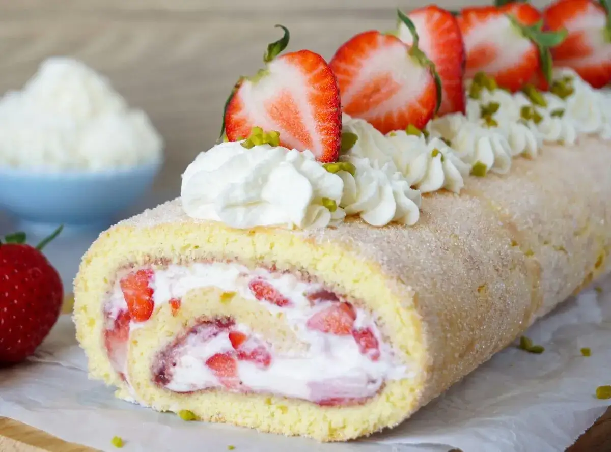 Saftige Erdbeer Biskuitrolle mit Sahne und frischen Erdbeeren, verziert mit Pistazien. Ein Genuss für jeden Anlass!