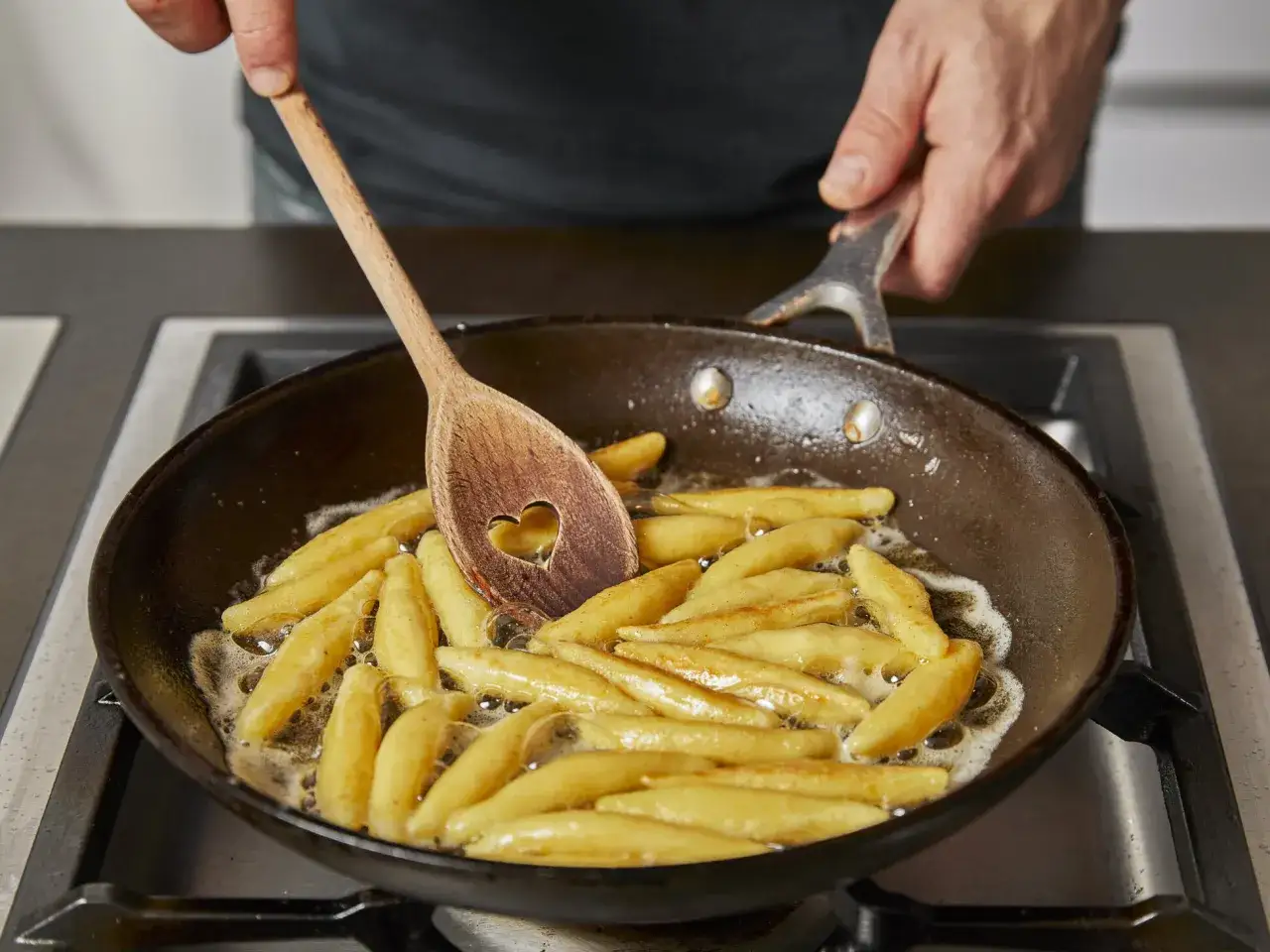 Schupfnudeln werden in einer Pfanne goldbraun gebraten. Ein Kochl&ouml;ffel mit Herzform r&uuml;hrt die Nudeln f&uuml;r das Schupfnudeln Rezept.