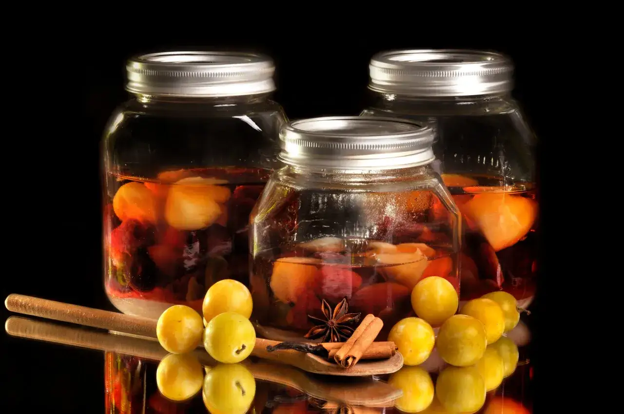 Drei Gläser mit Früchten in Alkohol, bereit für das Rumtopf Rezept nach Oma. Daneben liegen Zwetschgen, Zimt und Sternanis.