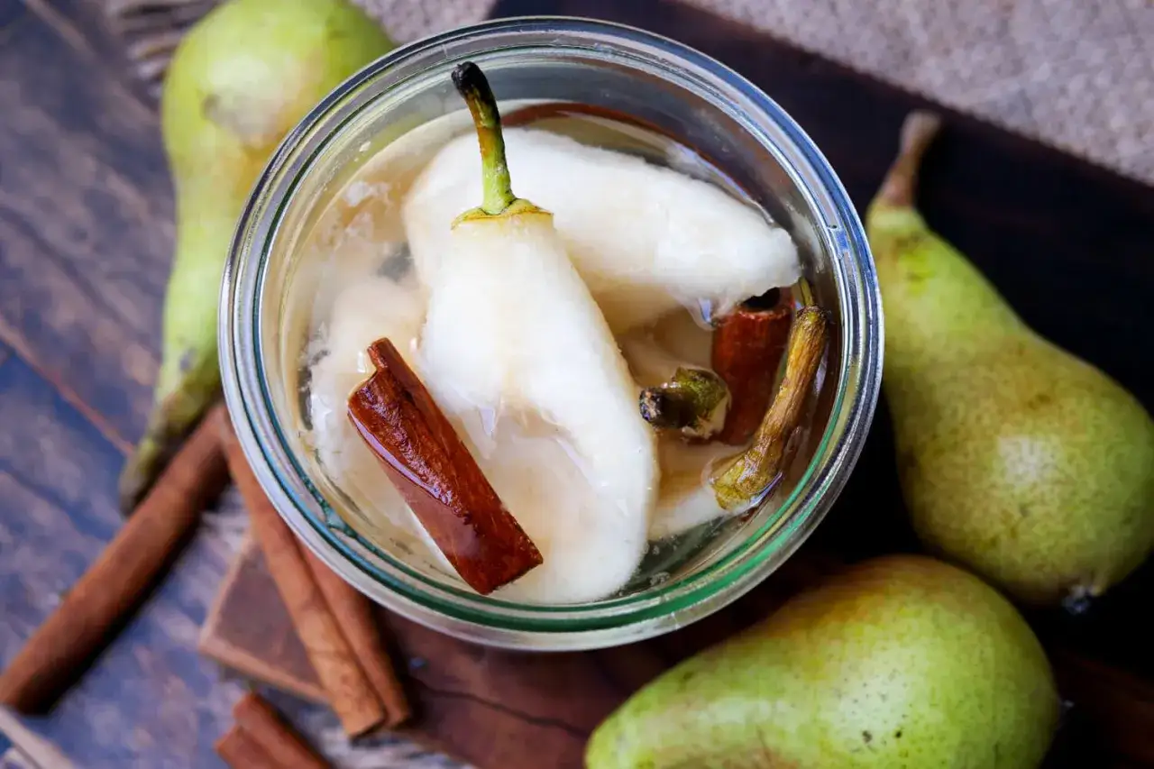 Gourmet-Birnen in Sirup mit Zimtstangen, bereit zum Einkochen. Frische Birnen und Gewürze auf rustikalem Holz.