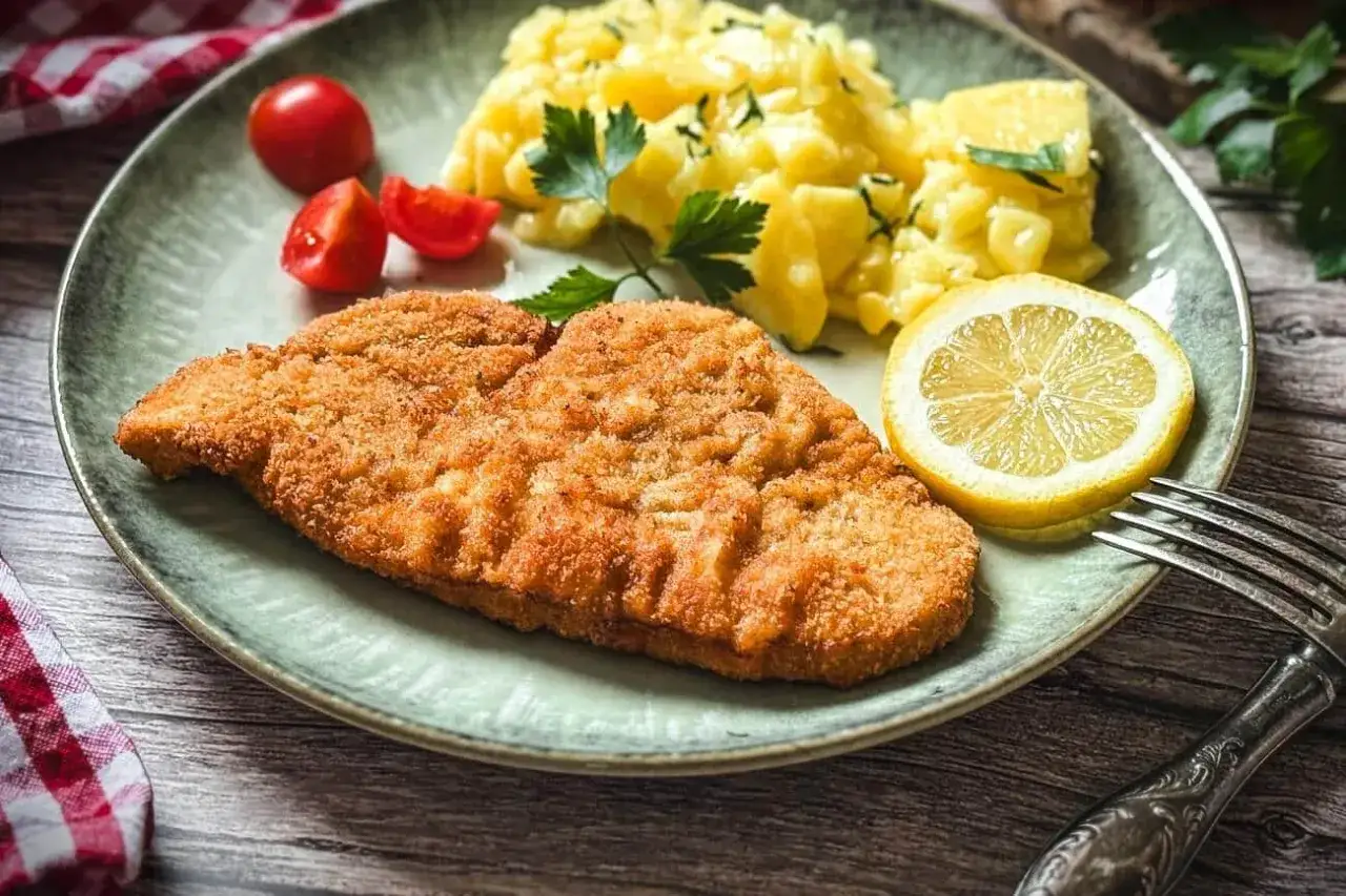 Perfekt gebratenes Putenschnitzel mit Kartoffelsalat, Tomaten und Zitrone auf einem Teller.