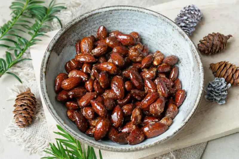Schüssel mit glasierten, gebrannten Mandeln, zubereitet im Airfryer. Dekoriert mit Tannenzapfen und Tannenzweigen.