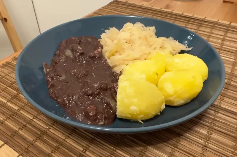 Ein Teller mit deftigem Essen: dunkle Soße, Sauerkraut und Salzkartoffeln. Erinnert an die gute, alte tote Oma.